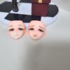 Two doll heads with detailed eyes and blush, displayed on a black-and-white checkered base